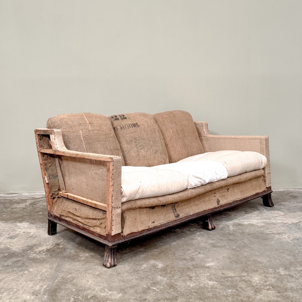 A French three-seater sofa featuring exposed timber framing, natural hessian sacking upholstery, hand-tacked trim, and turned front legs.