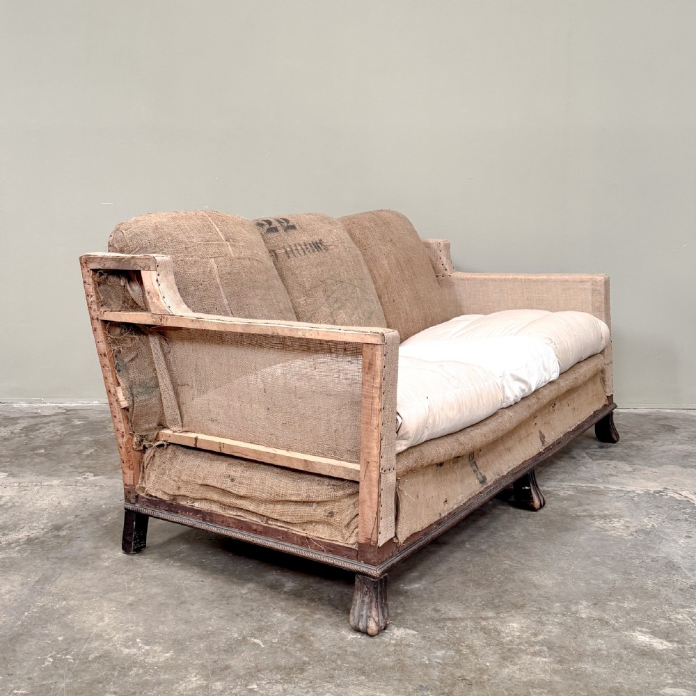 A French three-seater sofa featuring exposed timber framing, natural hessian sacking upholstery, hand-tacked trim, and turned front legs. View III