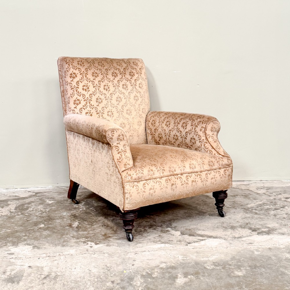 An Edwardian upholstered armchair with patterned beige damask fabric, rolled arms, turned front legs, and brass castors.