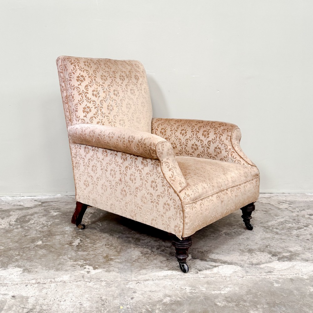 An Edwardian upholstered armchair with patterned beige damask fabric, rolled arms, turned front legs, and brass castors. View III