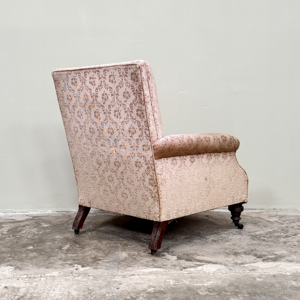 An Edwardian upholstered armchair with patterned beige damask fabric, rolled arms, turned front legs, and brass castors. View V