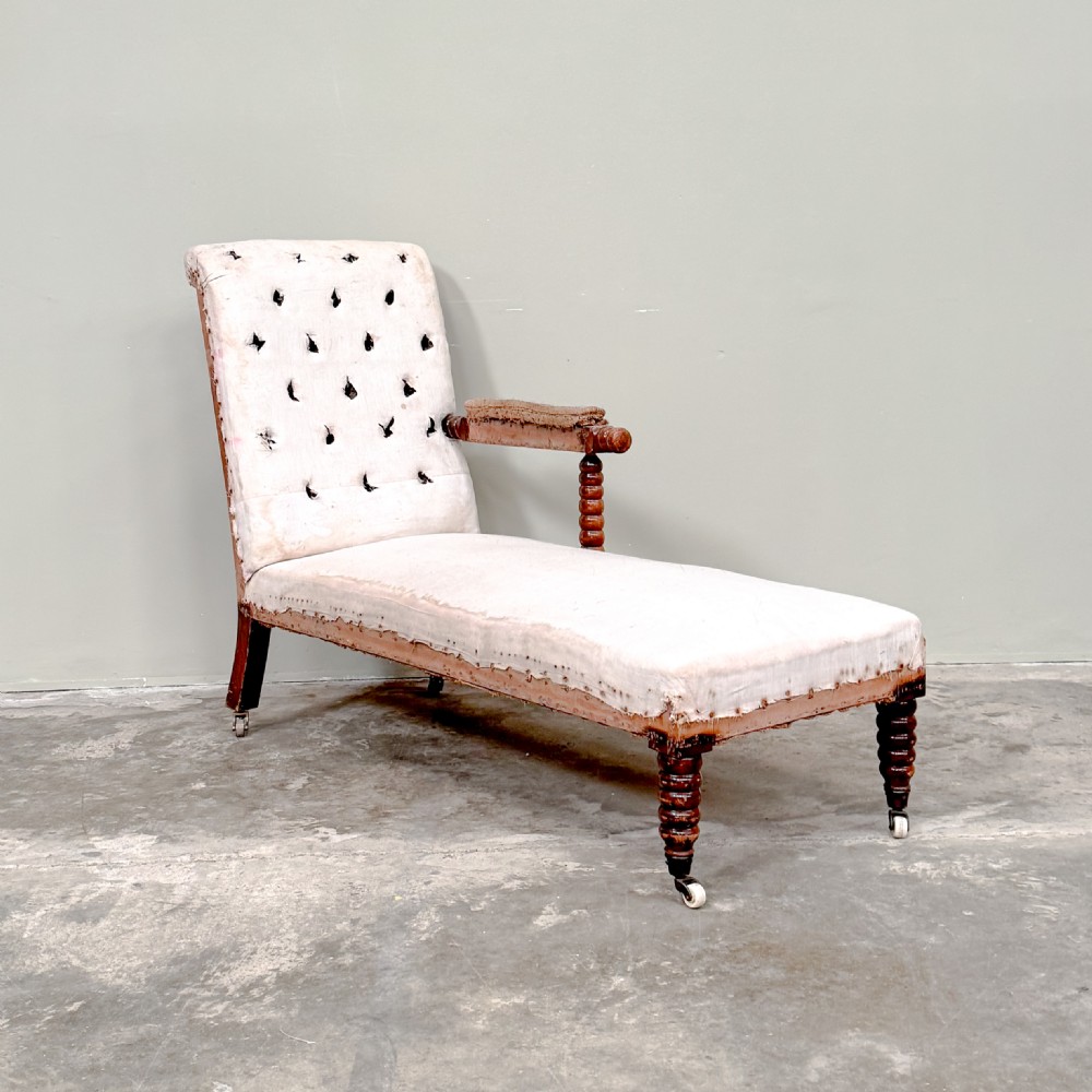 A 19th-century Victorian bobbin day bed featuring a single upholstered arm, button-tufted backrest, dark bobbin-turned legs, and castors.