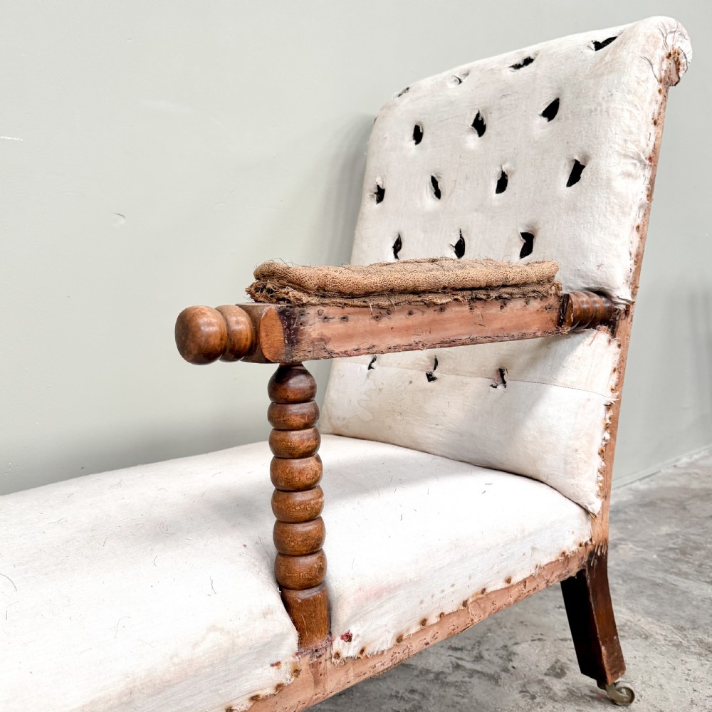 A 19th-century Victorian bobbin day bed featuring a single upholstered arm, button-tufted backrest, dark bobbin-turned legs, and castors. View V