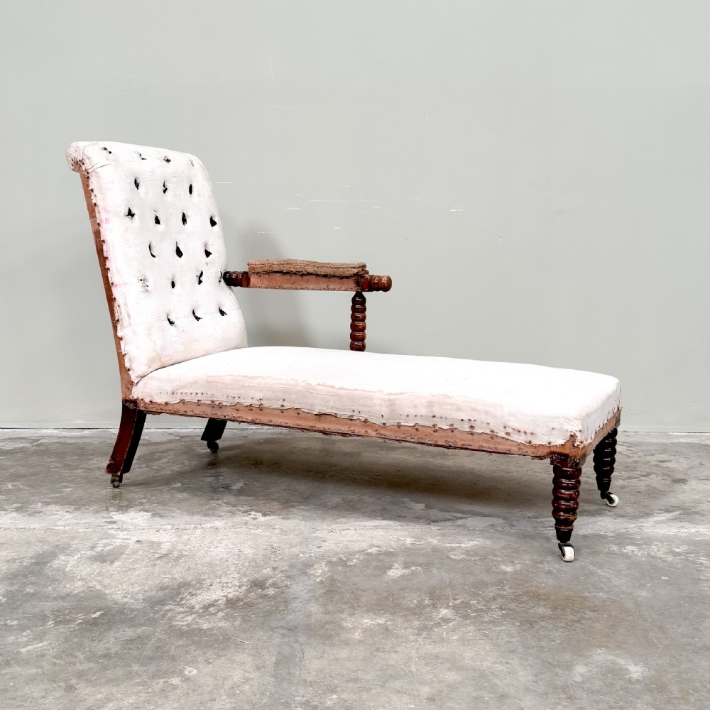 A 19th-century Victorian bobbin day bed featuring a single upholstered arm, button-tufted backrest, dark bobbin-turned legs, and castors. View VI