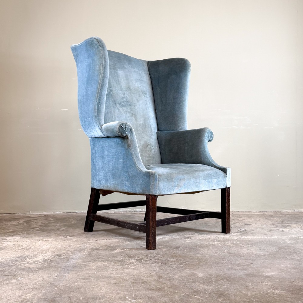 A high-backed Georgian wing chair upholstered in light blue velvet, supported by dark mahogany square legs with horizontal stretchers.