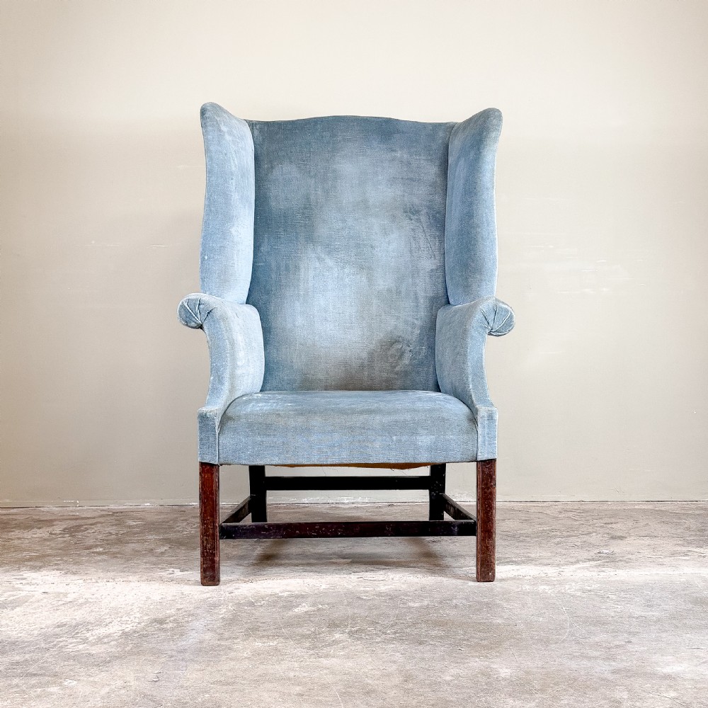 A high-backed Georgian wing chair upholstered in light blue velvet, supported by dark mahogany square legs with horizontal stretchers. View II