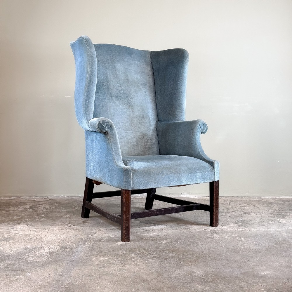 A high-backed Georgian wing chair upholstered in light blue velvet, supported by dark mahogany square legs with horizontal stretchers. View III