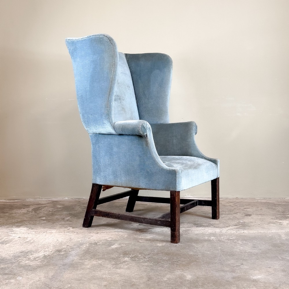 A high-backed Georgian wing chair upholstered in light blue velvet, supported by dark mahogany square legs with horizontal stretchers. View IV