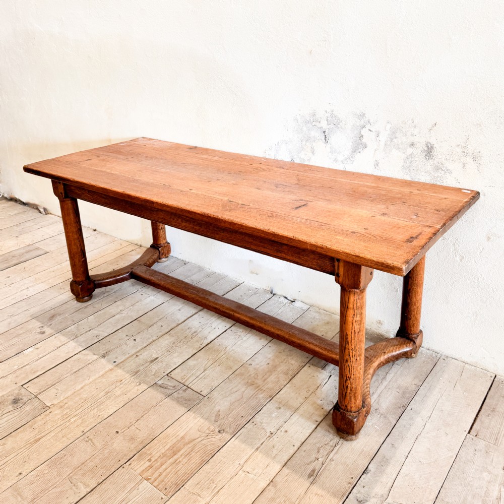 A rectangular solid oak refectory dining table featuring a plank top, barrel-turned legs, and a low central H-stretcher base.