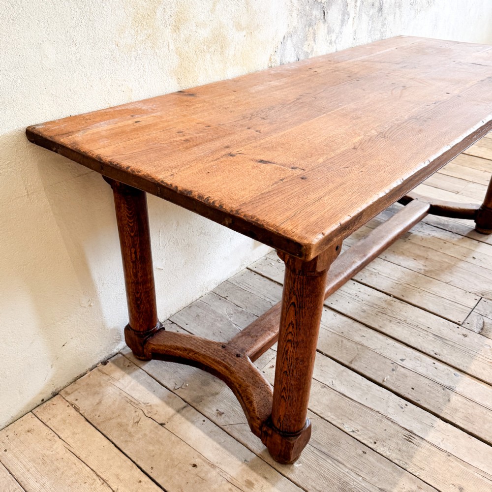 A rectangular solid oak refectory dining table featuring a plank top, barrel-turned legs, and a low central H-stretcher base. View III