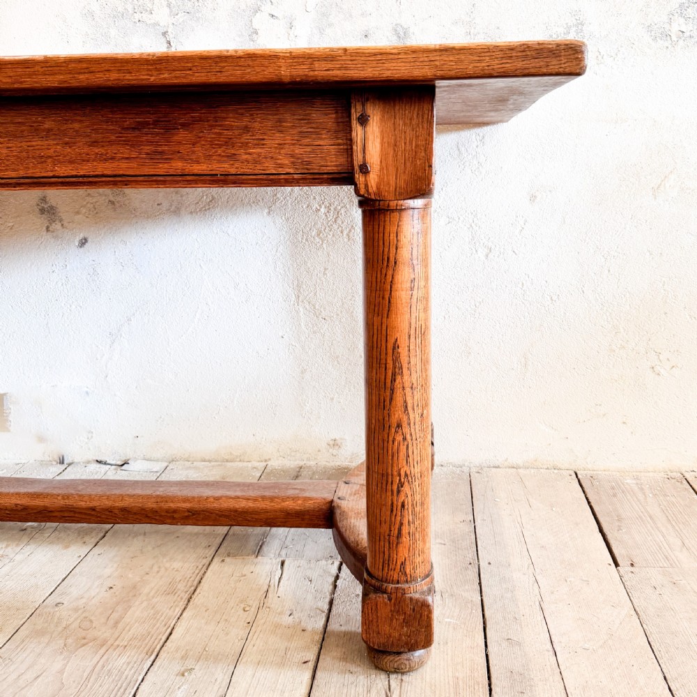 A rectangular solid oak refectory dining table featuring a plank top, barrel-turned legs, and a low central H-stretcher base. View IV