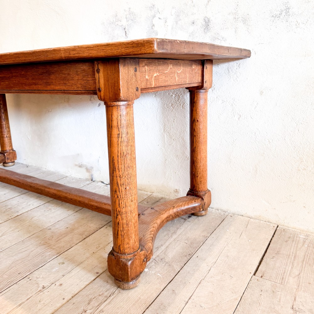 A rectangular solid oak refectory dining table featuring a plank top, barrel-turned legs, and a low central H-stretcher base. View V