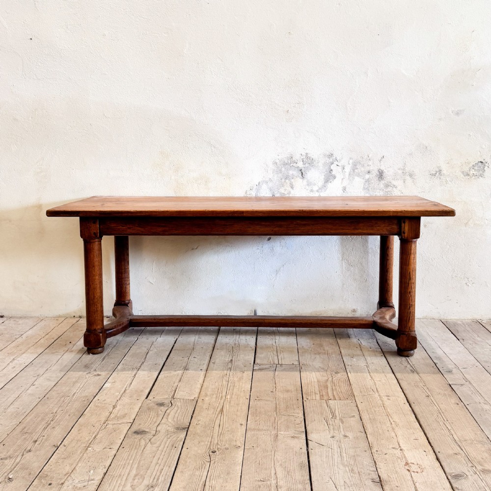 A rectangular solid oak refectory dining table featuring a plank top, barrel-turned legs, and a low central H-stretcher base. View VI