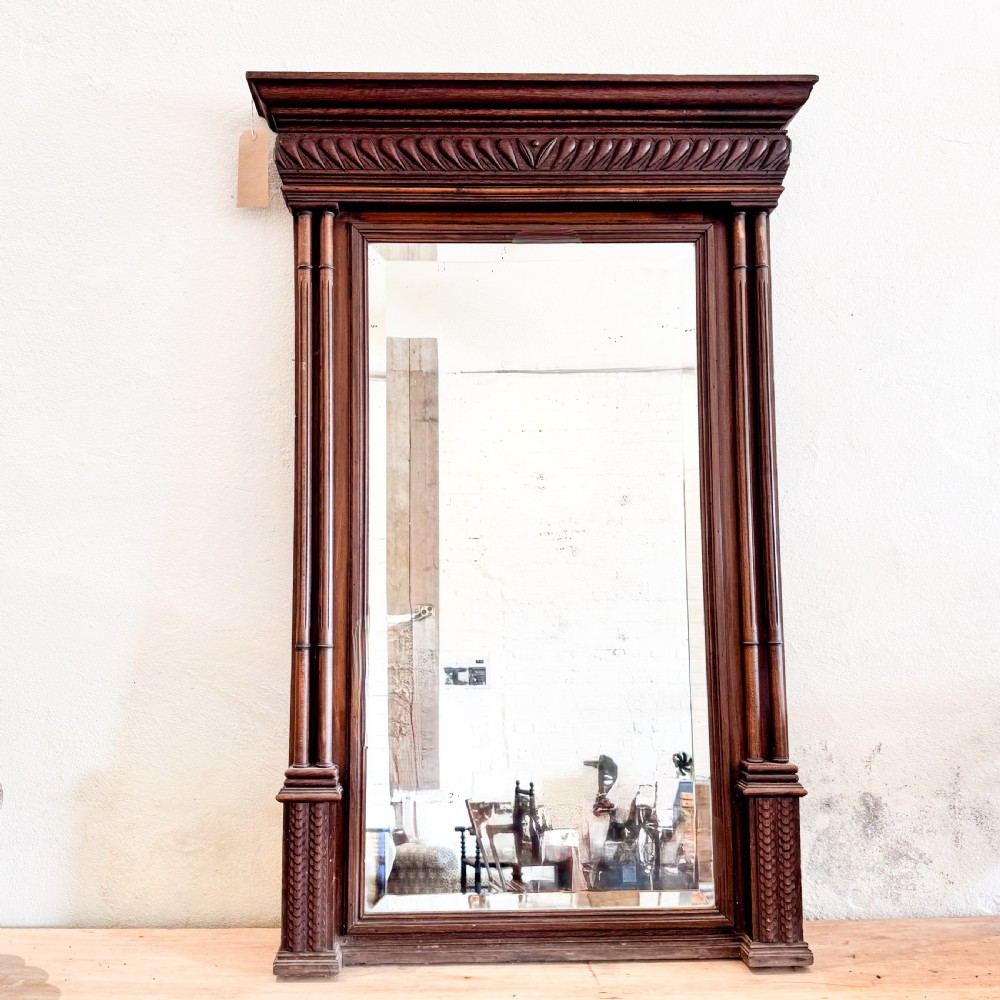A tall Victorian carved walnut overmantel mirror featuring an architectural cornice, fluted side columns, and an embellished upper frieze.