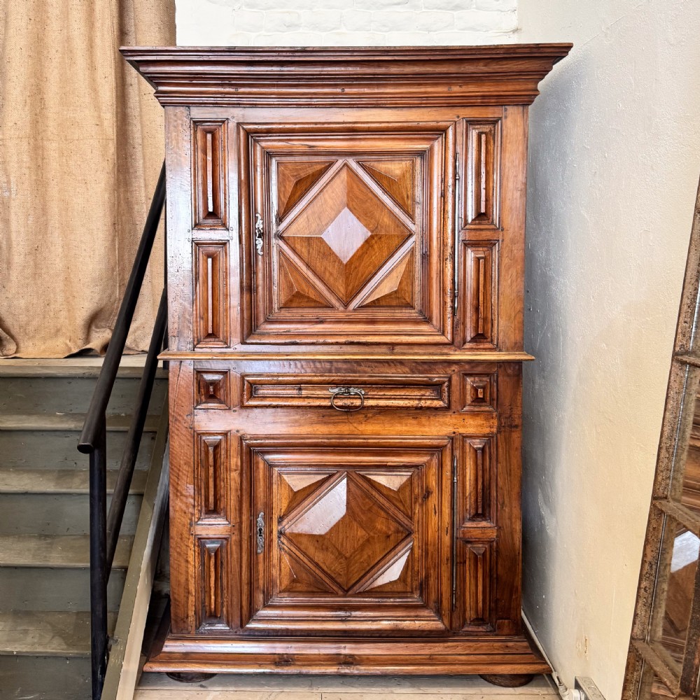 A tall two-tier Italian walnut cupboard featuring raised geometric diamond panels on two main cabinet doors, a central drawer, and heavy moulded cornices.