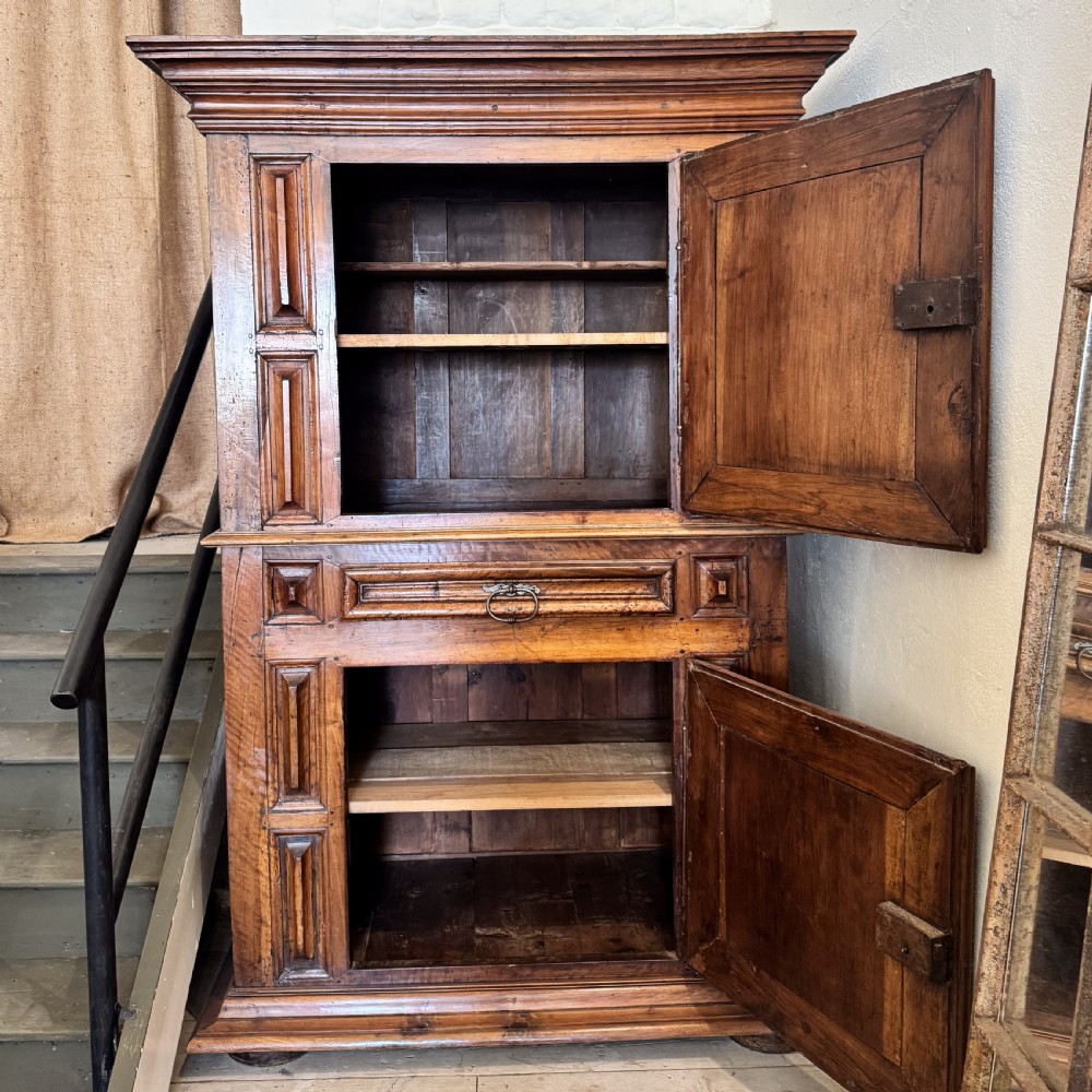 A tall two-tier Italian walnut cupboard featuring raised geometric diamond panels on two main cabinet doors, a central drawer, and heavy moulded cornices. View II