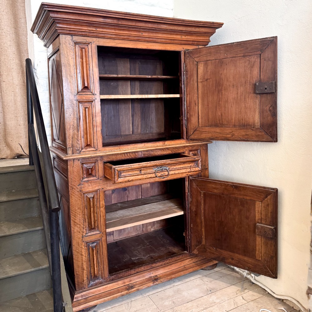 A tall two-tier Italian walnut cupboard featuring raised geometric diamond panels on two main cabinet doors, a central drawer, and heavy moulded cornices. View III