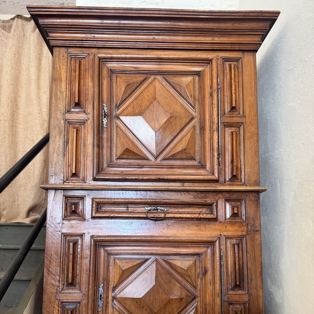 A tall two-tier Italian walnut cupboard featuring raised geometric diamond panels on two main cabinet doors, a central drawer, and heavy moulded cornices. View IV