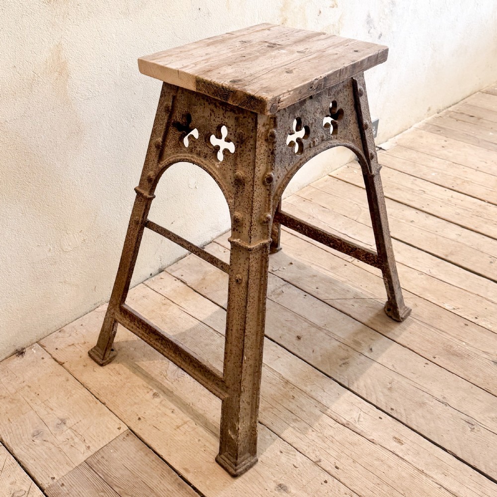 An industrial cast iron stand featuring trefoil arch cut-outs, a riveted frame, and a rectangular wooden top.