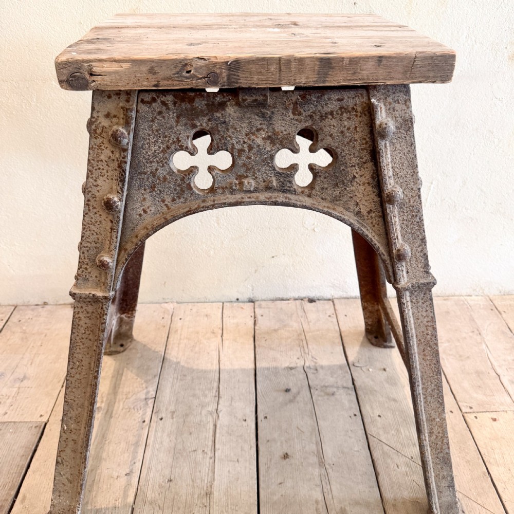An industrial cast iron stand featuring trefoil arch cut-outs, a riveted frame, and a rectangular wooden top. View III