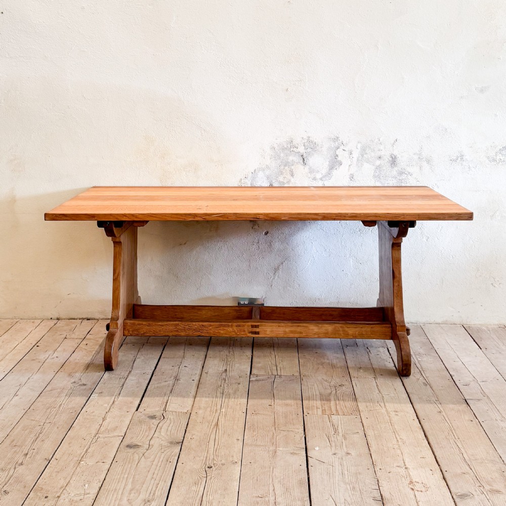 A solid oak dining table featuring a rectangular plank top resting on a trestle base with a central stretcher rail.