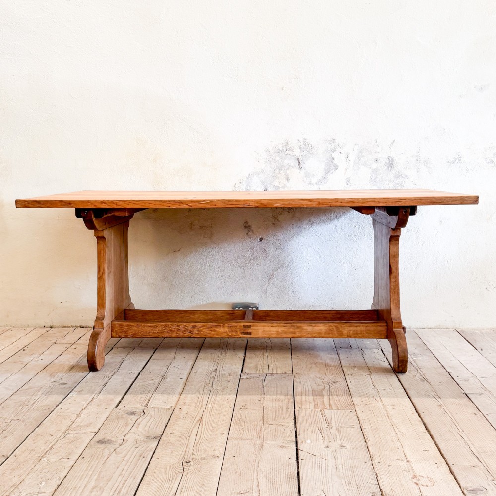 A solid oak dining table featuring a rectangular plank top resting on a trestle base with a central stretcher rail. View II