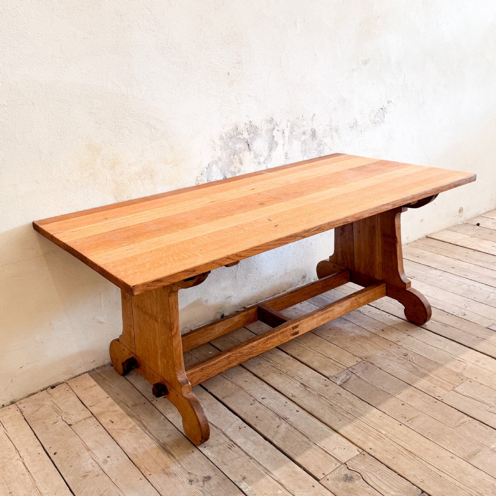 A solid oak dining table featuring a rectangular plank top resting on a trestle base with a central stretcher rail. View III