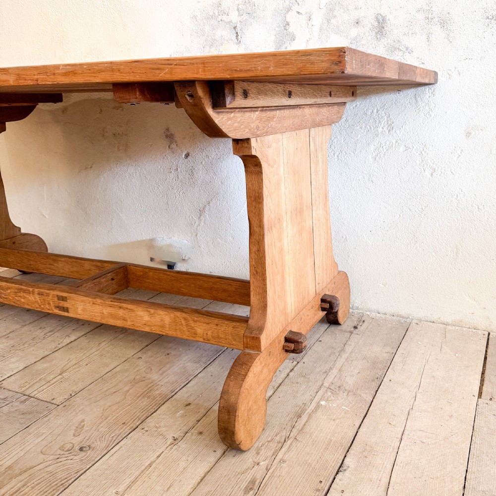 A solid oak dining table featuring a rectangular plank top resting on a trestle base with a central stretcher rail. View IV