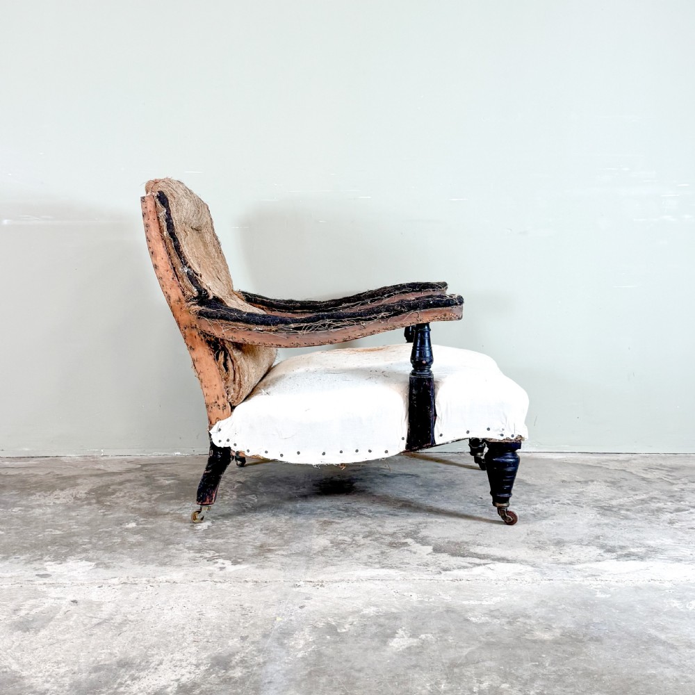An antique open arm library chair stripped to its calico and hessian lining, featuring black turned front legs with brass castors. View VI