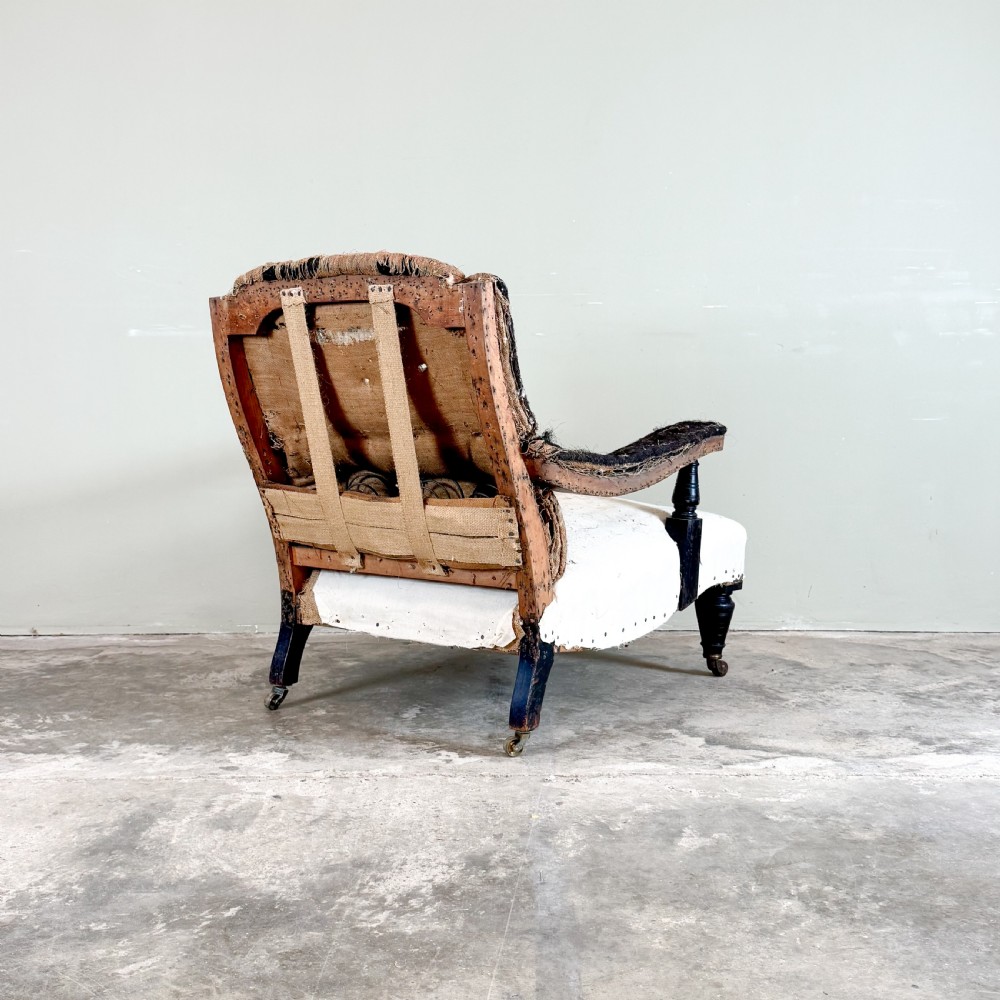An antique open arm library chair stripped to its calico and hessian lining, featuring black turned front legs with brass castors. View VII