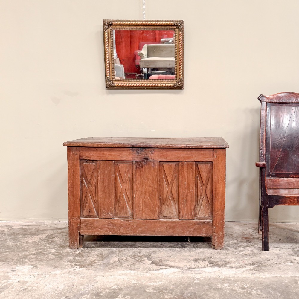 An 18th-century French provincial wooden coffer featuring hand-carved geometric front panels and a hinged top lid.