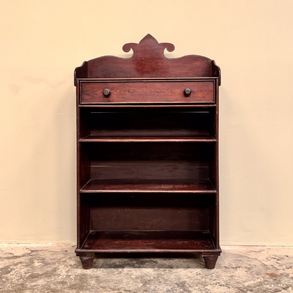An antique dark reddish-brown painted wooden open bookcase featuring a shaped pediment backboard, a single top drawer with wooden knobs, and four open shelves on turned bun feet. View II
