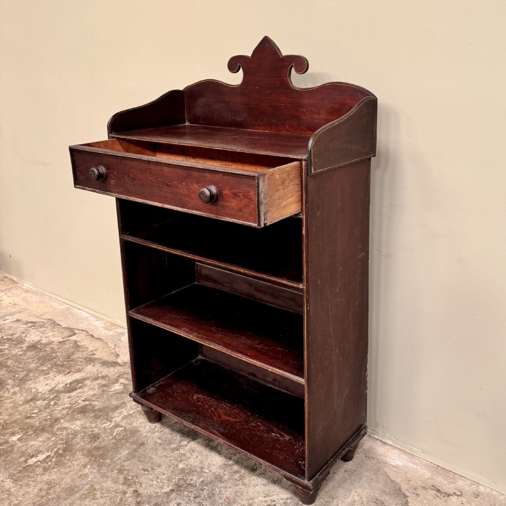 An antique dark reddish-brown painted wooden open bookcase featuring a shaped pediment backboard, a single top drawer with wooden knobs, and four open shelves on turned bun feet. View III