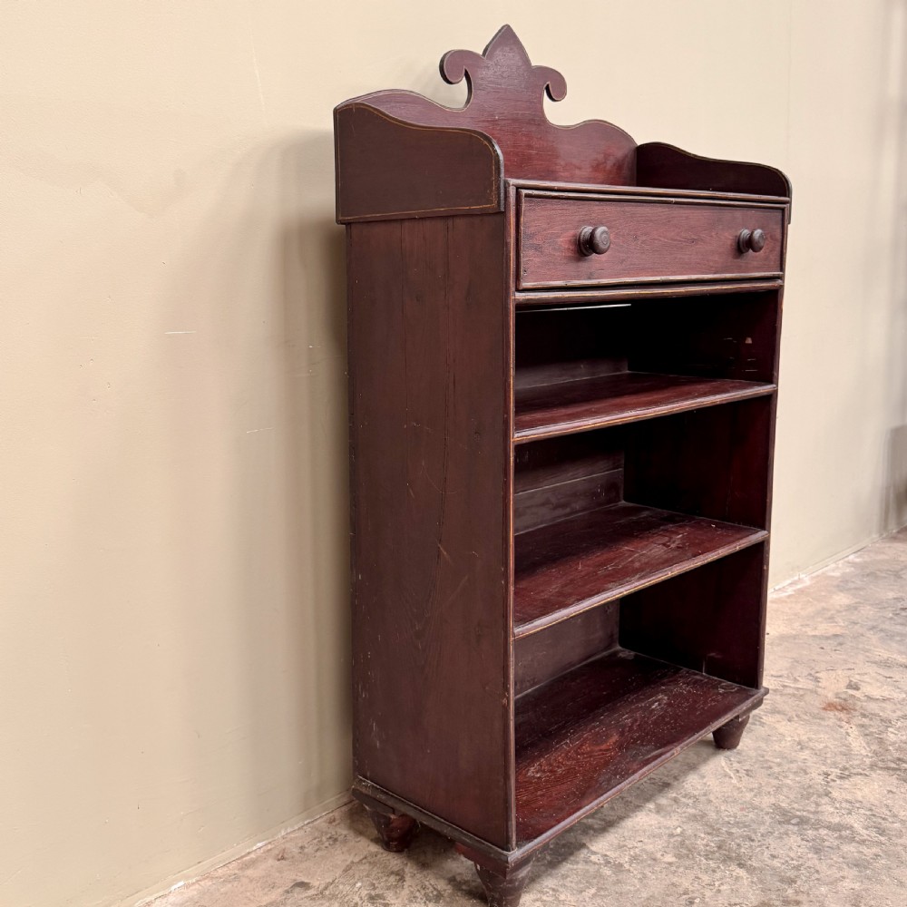 An antique dark reddish-brown painted wooden open bookcase featuring a shaped pediment backboard, a single top drawer with wooden knobs, and four open shelves on turned bun feet. View IV