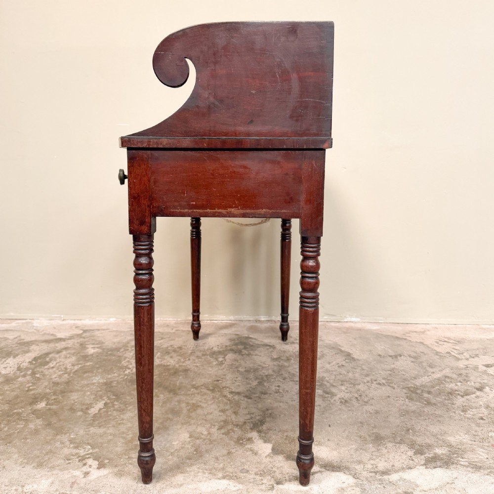 A Regency mahogany washstand featuring a raised scroll-shaped splashback gallery, two frieze drawers with round brass knobs, and four slender turned legs. View VI