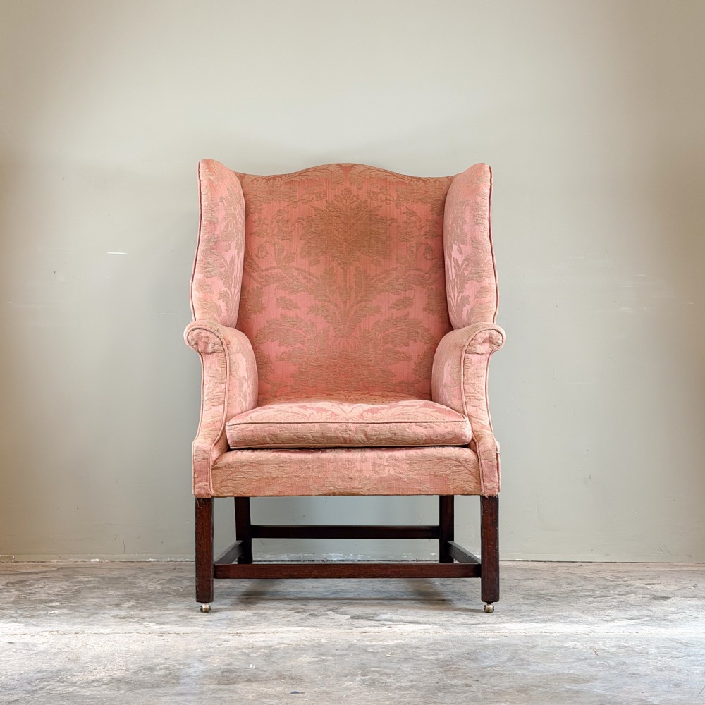A Georgian wingback armchair upholstered in patterned terracotta damask fabric with dark mahogany legs and brass castors. View II