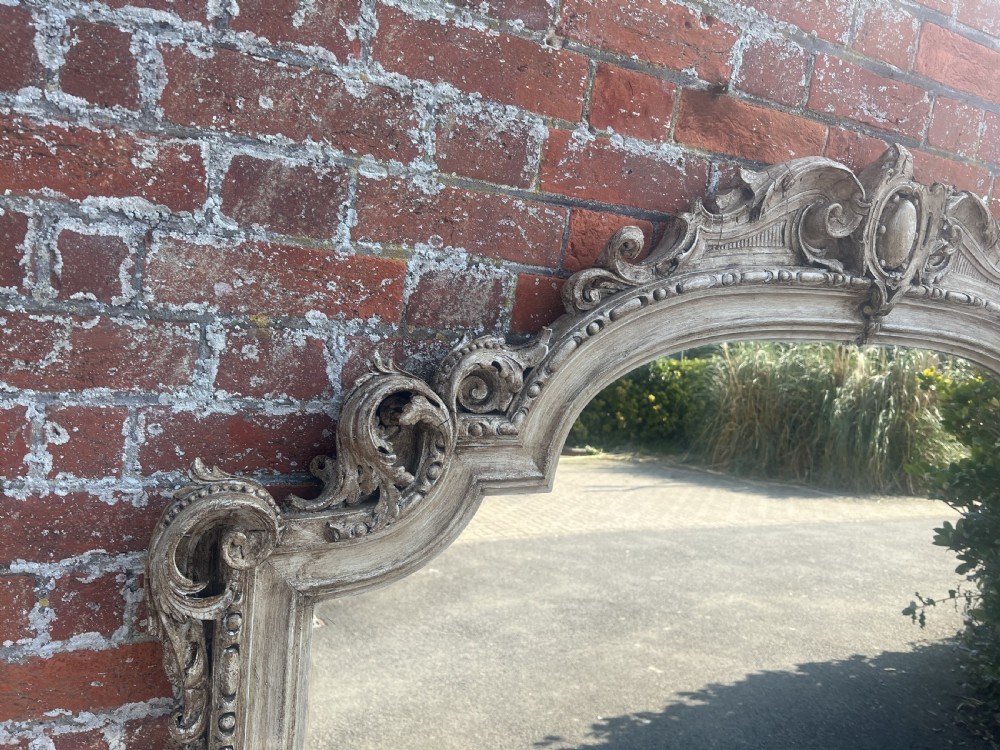 A large 19th-century painted wooden overmantel mirror featuring an arched frame topped with ornate carved scrollwork and a central oval medallion. View IV
