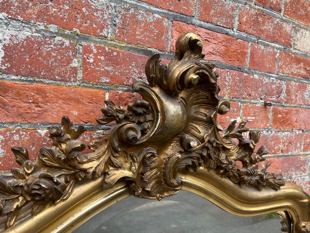 A large 19th-century French arched wall mirror featuring an ornate gold leaf carved gesso frame crowned with a foliate rococo crest. View VI