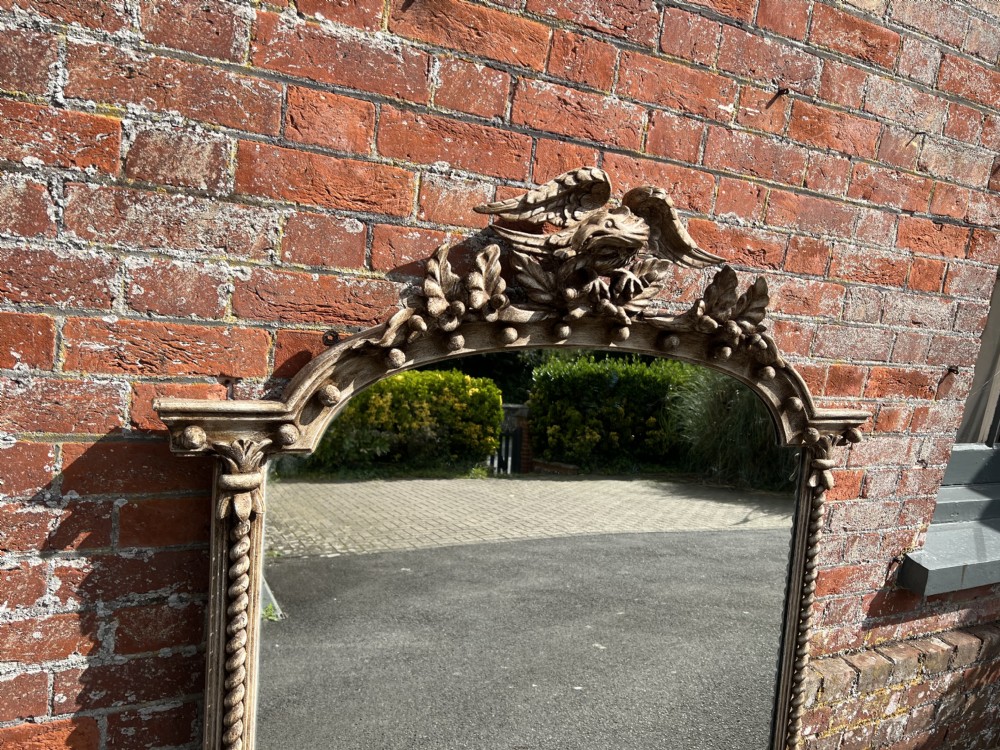 A large nineteenth-century arched overmantel mirror featuring a carved eagle cresting motif, rope twist column sides, and a distressed off-white painted finish. View V