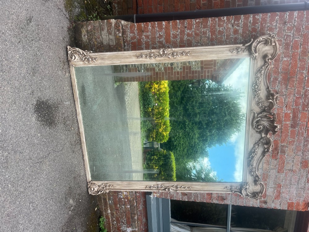 A large 19th-century French rectangular wall mirror featuring an off-white distressed painted frame with ornate carved gesso cresting and floral details. View VIII