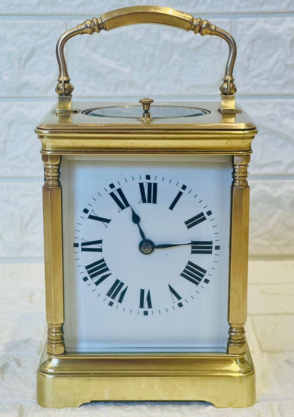 A rectangular brass carriage clock featuring a hinged carrying handle, bevelled glass panels, a top repeat button, and a white enamel dial with black Roman numerals.