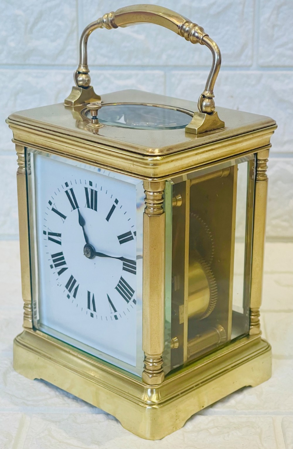 A rectangular brass carriage clock featuring a hinged carrying handle, bevelled glass panels, a top repeat button, and a white enamel dial with black Roman numerals. View II
