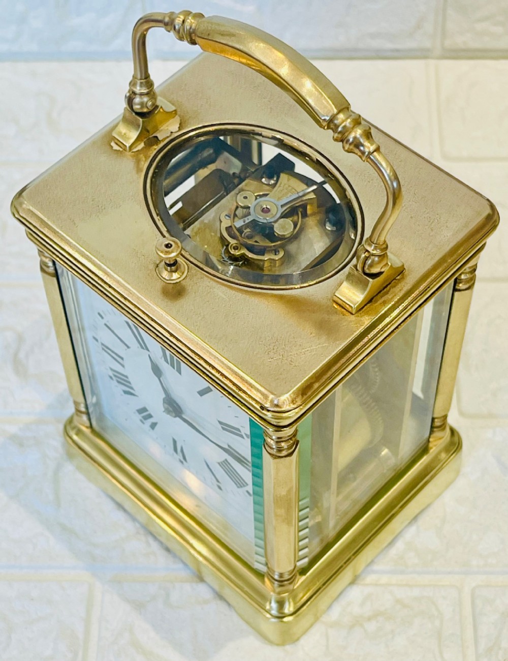 A rectangular brass carriage clock featuring a hinged carrying handle, bevelled glass panels, a top repeat button, and a white enamel dial with black Roman numerals. View III