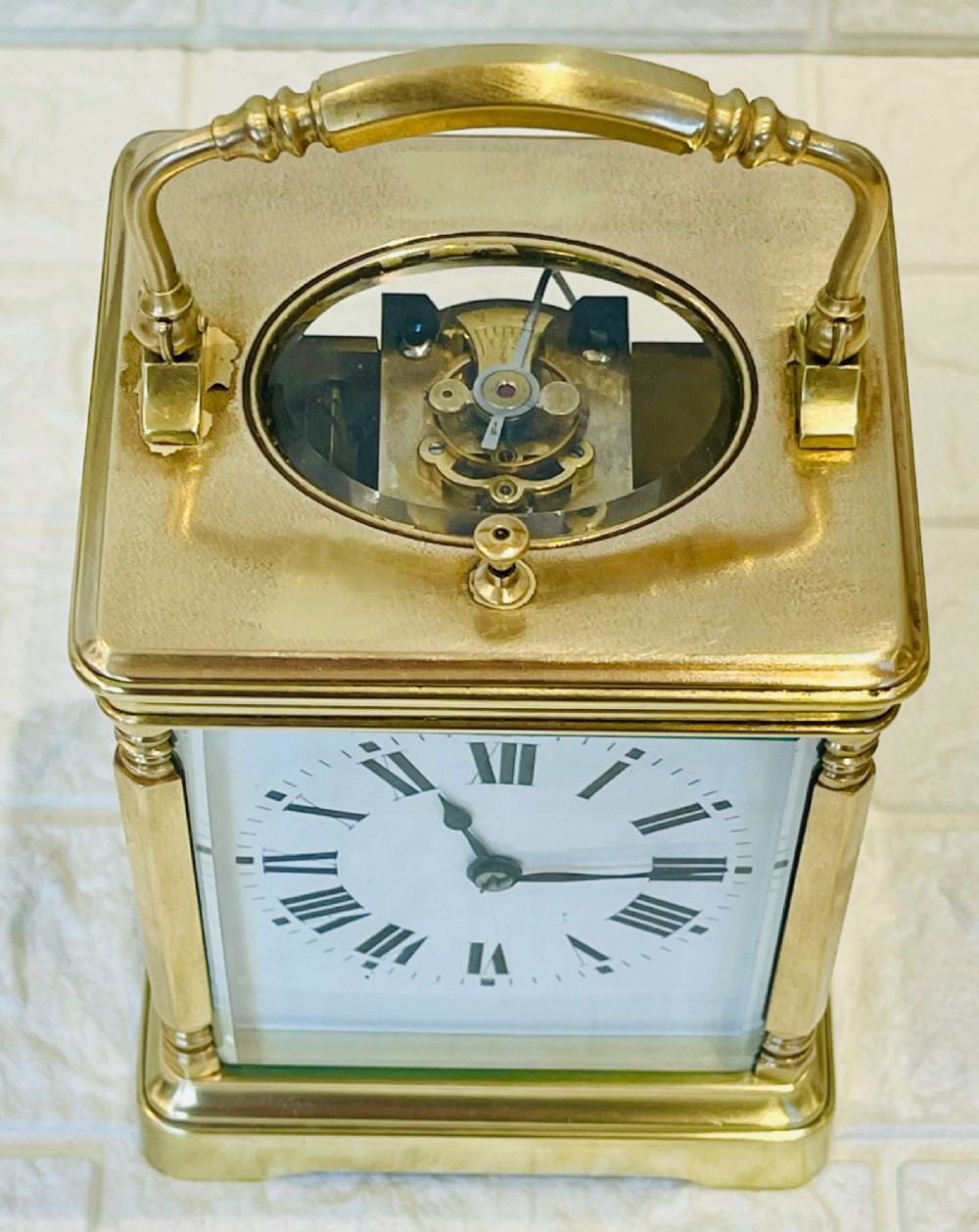 A rectangular brass carriage clock featuring a hinged carrying handle, bevelled glass panels, a top repeat button, and a white enamel dial with black Roman numerals. View IV