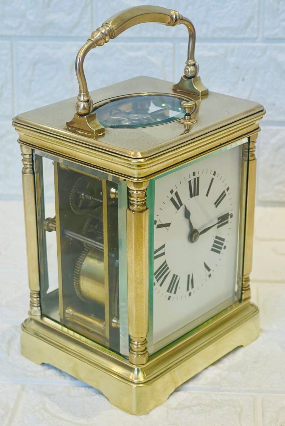 A rectangular brass carriage clock featuring a hinged carrying handle, bevelled glass panels, a top repeat button, and a white enamel dial with black Roman numerals. View V