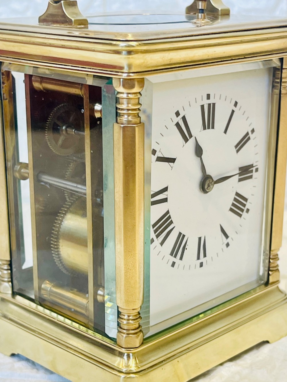 A rectangular brass carriage clock featuring a hinged carrying handle, bevelled glass panels, a top repeat button, and a white enamel dial with black Roman numerals. View VI