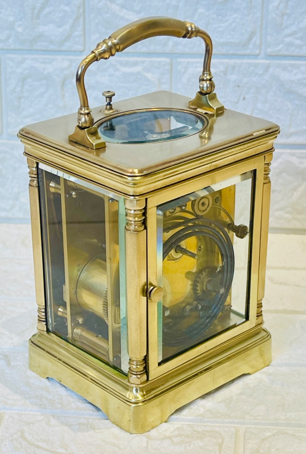 A rectangular brass carriage clock featuring a hinged carrying handle, bevelled glass panels, a top repeat button, and a white enamel dial with black Roman numerals. View VII