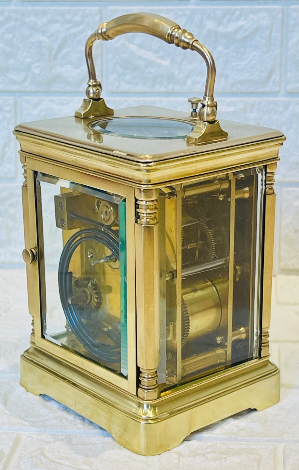 A rectangular brass carriage clock featuring a hinged carrying handle, bevelled glass panels, a top repeat button, and a white enamel dial with black Roman numerals. View VIII