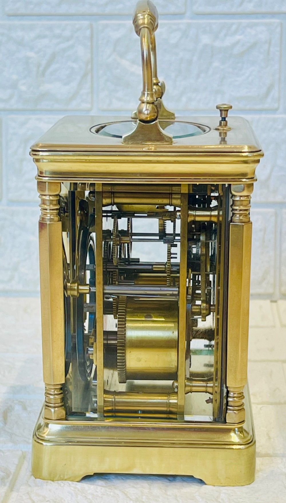 A rectangular brass carriage clock featuring a hinged carrying handle, bevelled glass panels, a top repeat button, and a white enamel dial with black Roman numerals. View IX