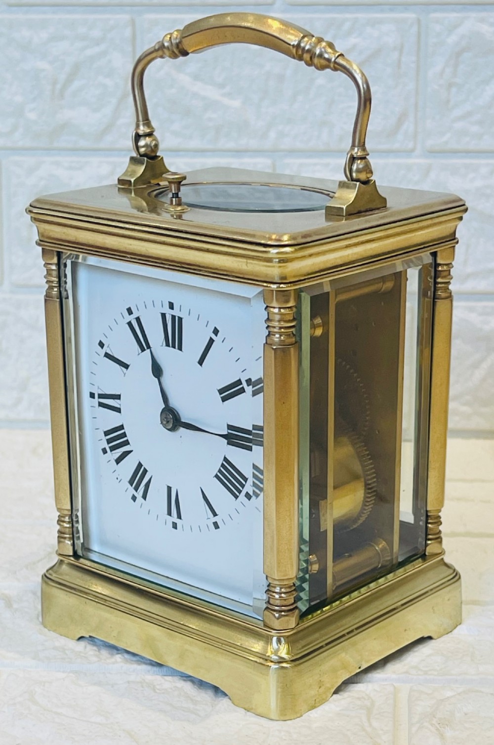 A rectangular brass carriage clock featuring a hinged carrying handle, bevelled glass panels, a top repeat button, and a white enamel dial with black Roman numerals. View X